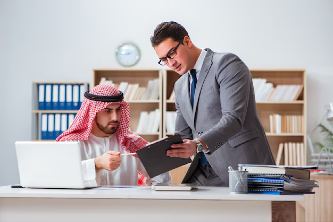 setup business in uae - Two professionals in an office, one in traditional Arab attire and the other in a suit, discussing over a document.