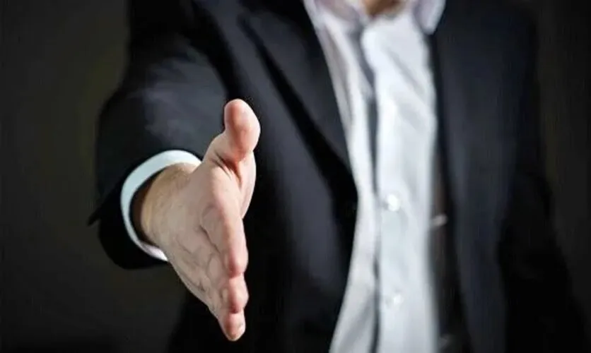  business set up companies in dubai - Man in a suit extending a handshake with focus on his hand.