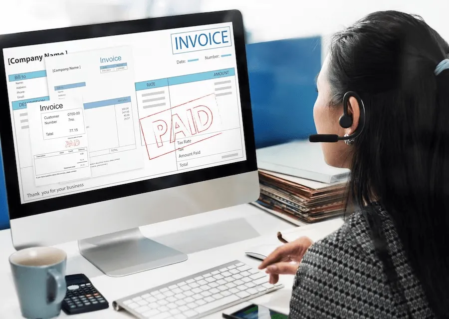 business setup services in dubai - Woman with headset views a 'PAID' invoice on computer screen in an office setting.