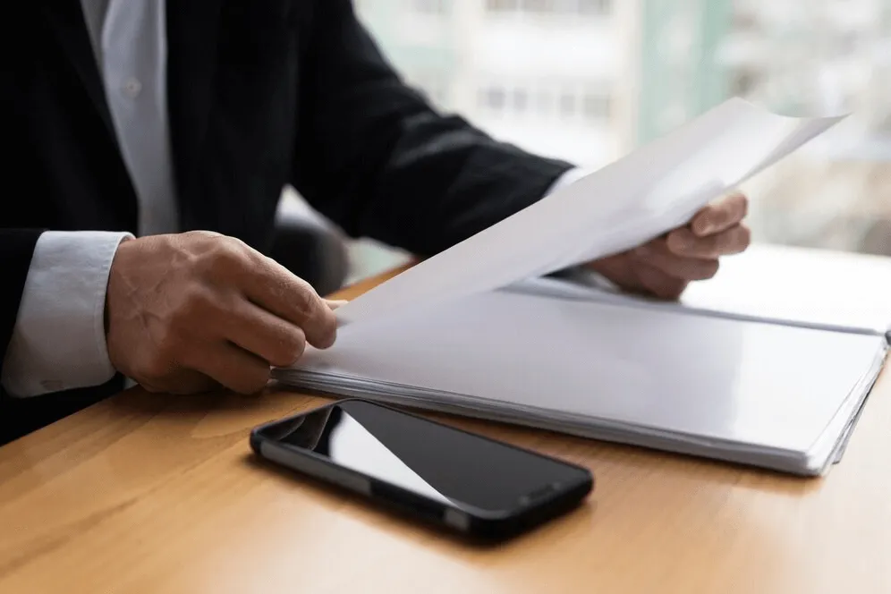 business setup services in dubai -Person in a suit reviewing documents with a smartphone on the table.