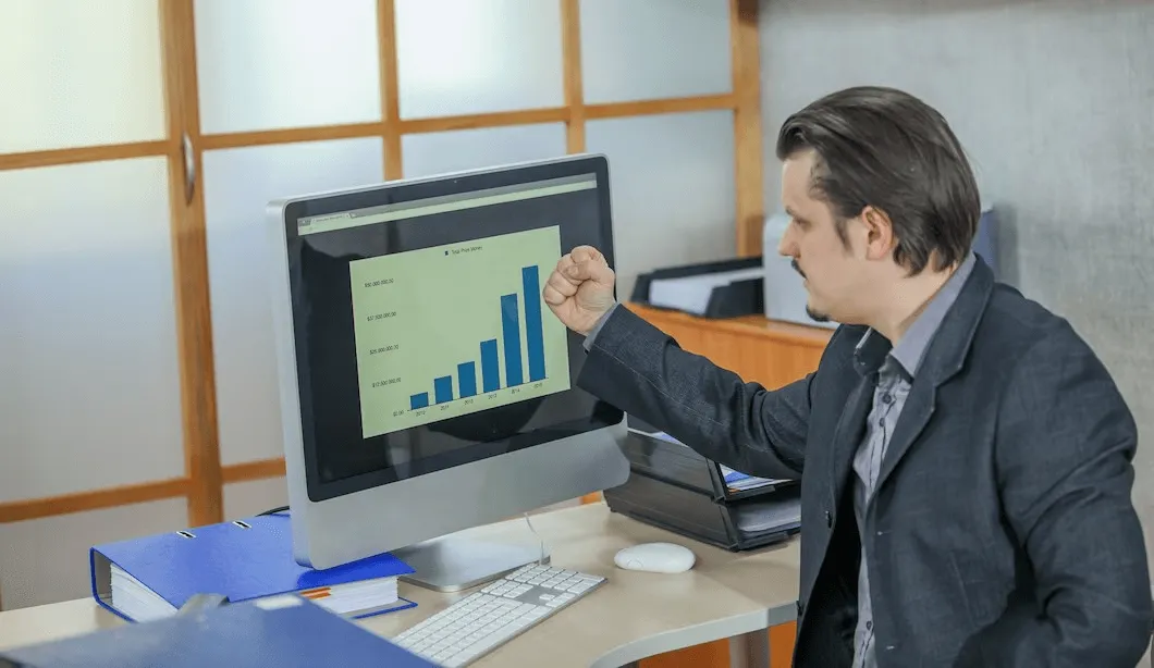  business setup services in dubai- Person in a suit pointing at a bar graph on a desktop computer screen in an office.