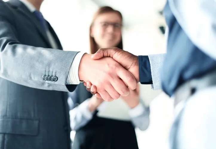 Business Setup Consultants in Dubai - Two professionals in suits shaking hands, with a blurred office background. 