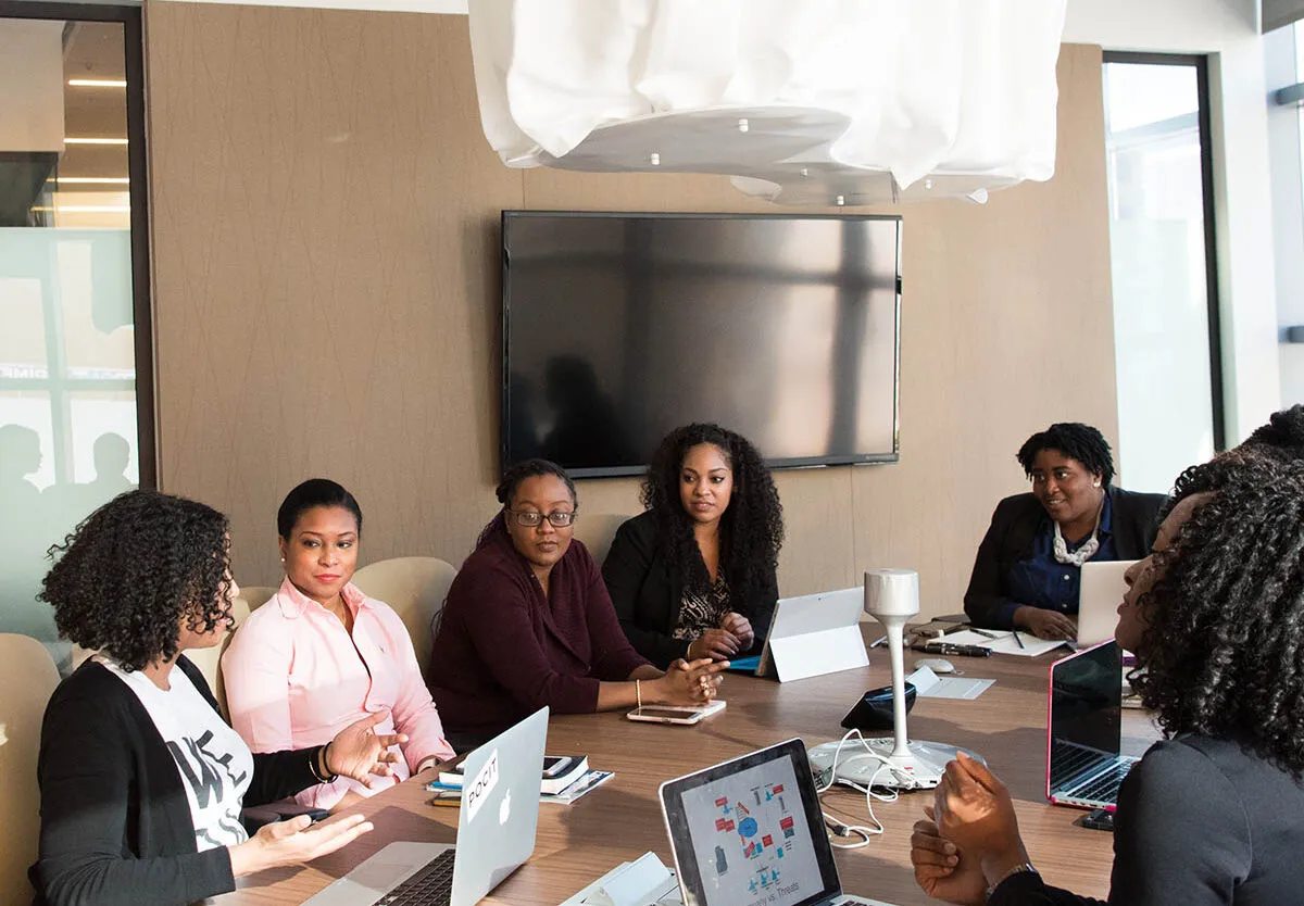 Business Setup Consultants in Dubai - Group of professionals in a meeting around a table with laptops and a blank screen.