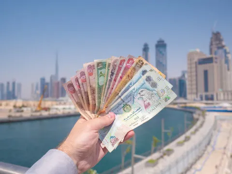  business setup services in dubai- Hand holding UAE currency with skyscrapers and clear sky in the background.