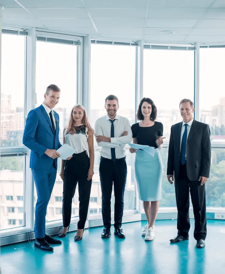 Company Setup Dubai - Five professionals with documents standing in a bright office with large windows.