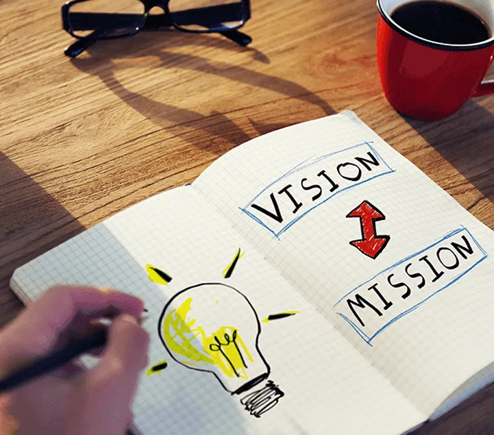  Company Setup Dubai - Notebook with 'VISION MISSION' text and lightbulb drawing, coffee mug, and glasses on a table.